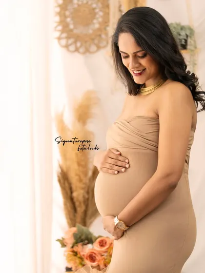 A simple, elegant portrait in a fitted nude gown, capturing a quiet moment of connection with the baby bump.