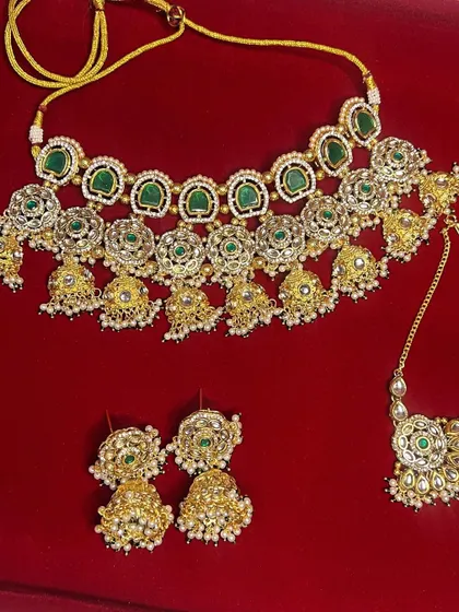 A flat-lay image of the green choker, earrings, and maang tikka, showing all the pieces you get when you rent this popular set.
