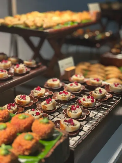 A beautiful array of canapés on a buffet line, including savory bites topped with pomegranate seeds. The variety and meticulous arrangement demonstrate the scale and quality of our catering.