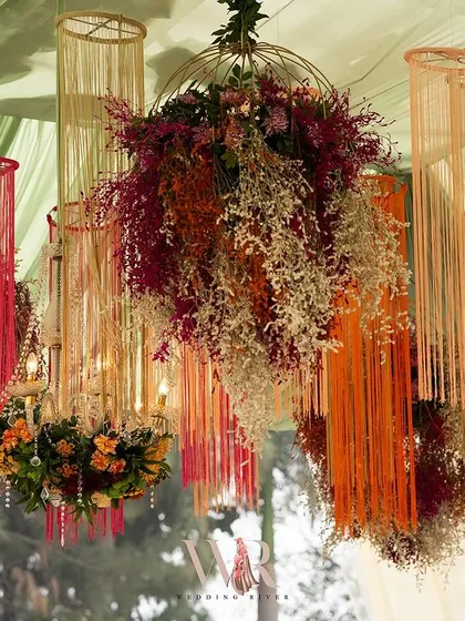A stunning ceiling installation featuring chandeliers wrapped in colorful threads and dried flowers. This creative and textural element was a major highlight of the bohemian-themed decor.