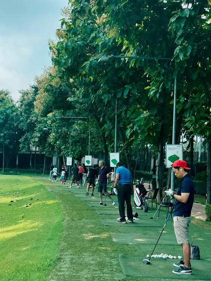 A player takes a moment to prepare, surrounded by the lush greenery and fellow golfers on a busy afternoon.