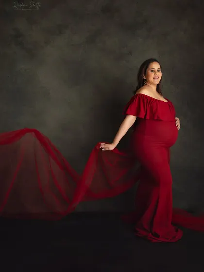 The deep red of this off-shoulder gown against a dark, moody backdrop creates a dramatic and powerful portrait. The flowing fabric adds a touch of softness and movement.