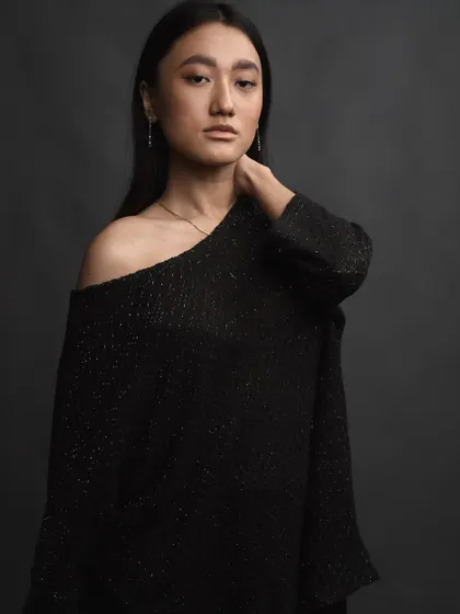 A quiet and elegant portrait against a dark, textured backdrop. The off-the-shoulder top and simple styling draw attention to the graceful line of the neck and shoulders.