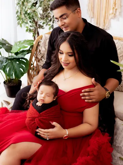 A beautiful family portrait with a newborn baby. The parents look on lovingly at their sleeping child, wrapped snugly in red.