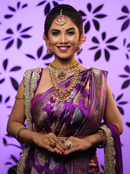 A full-length view of the bride in her purple saree, showcasing the complete styling from head to toe. The draping is neat and accentuates her figure.