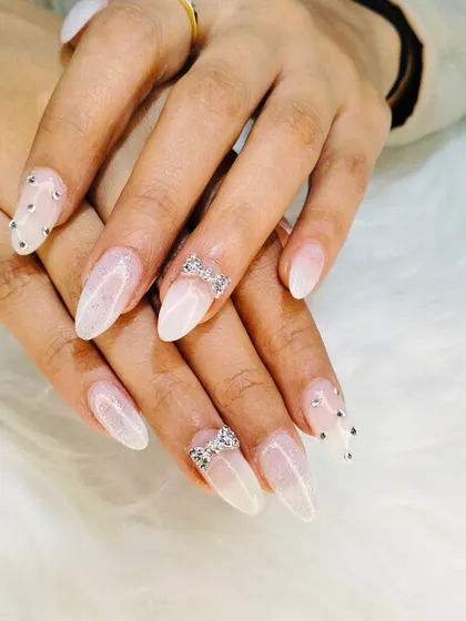 A different angle of the elegant milky white extensions, highlighting the sharp stiletto shape and the intricate rhinestone bow details.