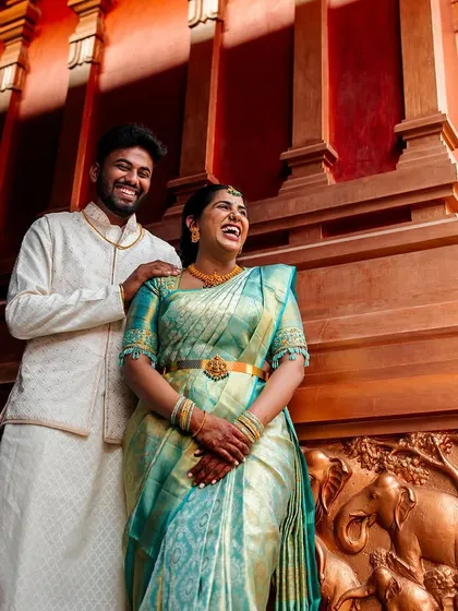 A candid laugh during an engagement shoot. The rich wooden backdrop with elephant carvings adds a traditional touch to this vibrant, happy portrait.