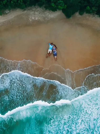 An aerial drone shot of a couple on a secluded beach, showcasing a unique perspective on their pre-wedding shoot. We use advanced techniques to create visually stunning and creative images.