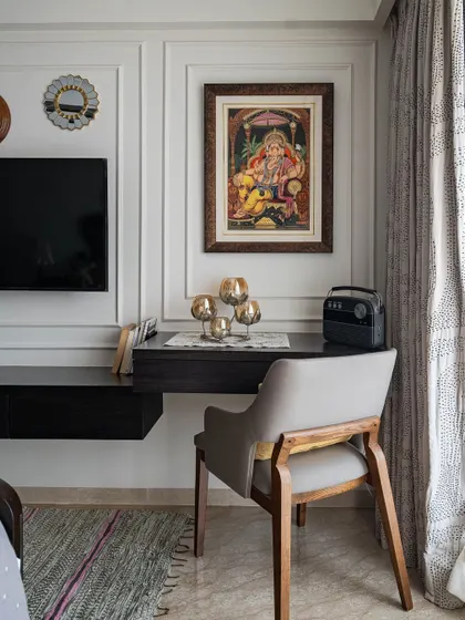 A compact and functional study nook carved out in a bedroom. The floating desk and classic chair are placed beside the TV unit, with traditional Indian art adding a touch of cultural elegance.