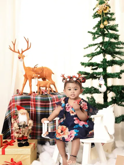 A festive Christmas portrait. This little girl, wearing reindeer antlers, sits on a rocking horse in our beautifully decorated holiday set.