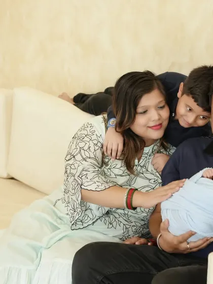 A candid family moment filled with love and affection. The older brother peeks over the couch, excited to be close to his new sibling.