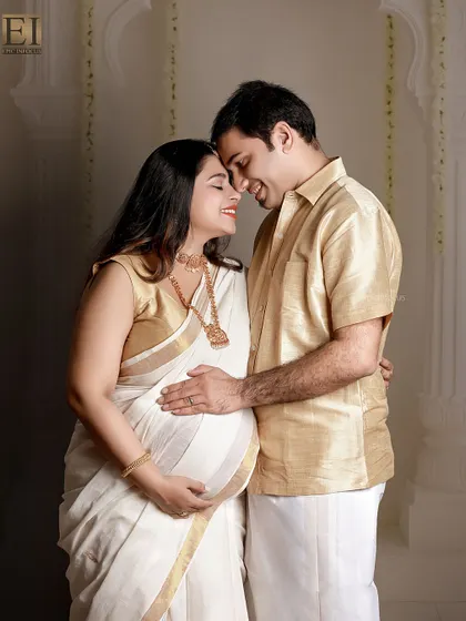 Celebrating heritage and love. This couple's portrait, featuring a traditional white and gold Kerala saree, beautifully blends cultural elegance with the intimacy of the maternity journey in a classic studio setting.