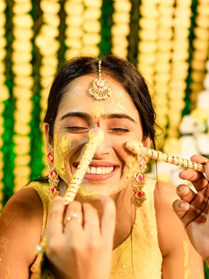 A playful and funny moment from a Haldi ceremony, where the bride is being teased with food, her face covered in turmeric.