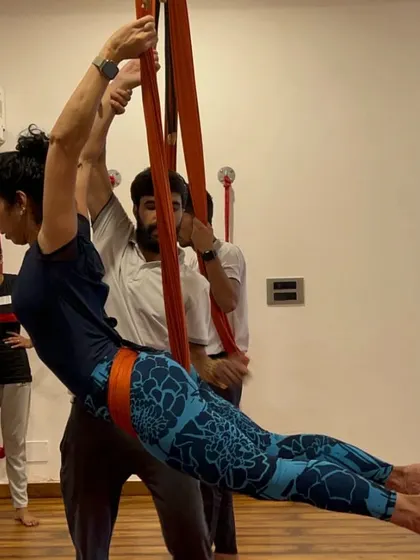 Learning to teach Aerial Yoga requires hands-on practice. Here, an instructor guides a trainee through a supported pose.