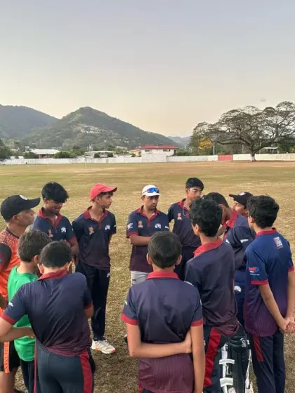 A team huddle during our international tour in Trinidad. Our coach strategizes with the team against a scenic mountain backdrop.