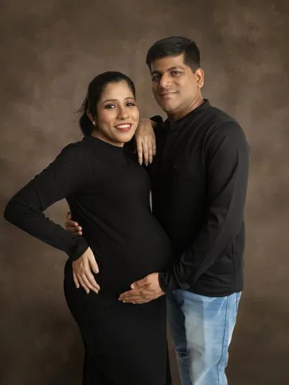 A classic standing pose for a couple. The simple, dark outfits against a textured brown backdrop create a warm and timeless portrait.