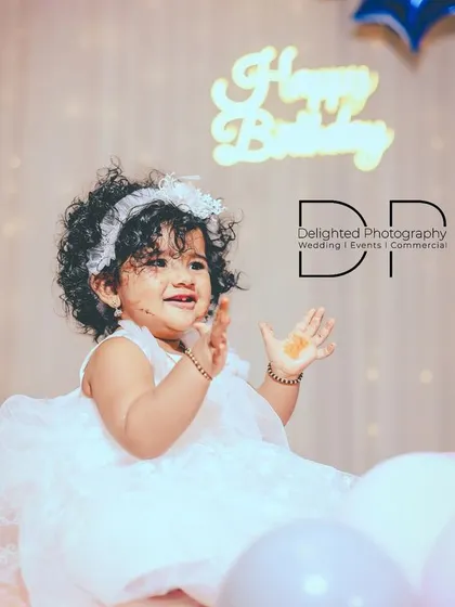 A precious photo of a one-year-old birthday girl clapping her hands with joy, surrounded by pastel balloons and a 'Happy Birthday' sign.