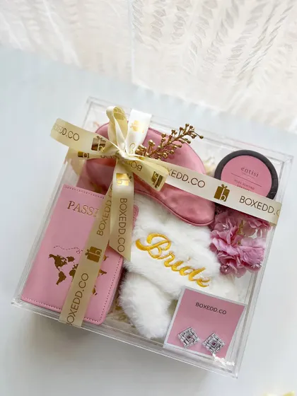 Forget the old shagun ka lifafa. This modern acrylic gift box for the bride-to-be is filled with travel essentials like a passport cover, comfy 'Bride' slippers, a silk eye mask, and jewelry.