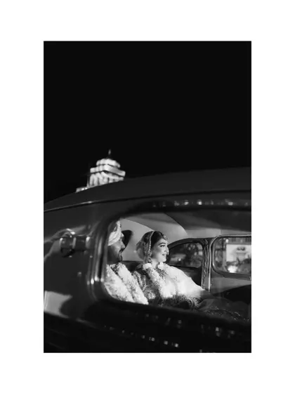 A classic, cinematic black and white shot of Sanskriti and Rahul in a vintage car at their Jaipur wedding.