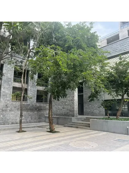 A paved plaza within the hostel complex, surrounded by trees. These open spaces are designed as extensions of the indoor common areas, encouraging students to gather outdoors.