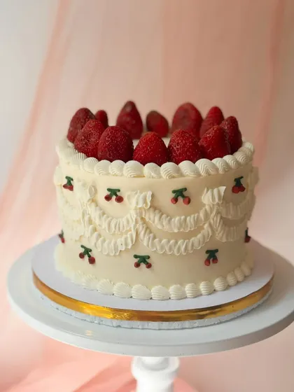 A delightful vintage-style cake combining two favourites. It features classic Lambeth swag piping with tiny cherry details and is topped with a pile of fresh strawberries.