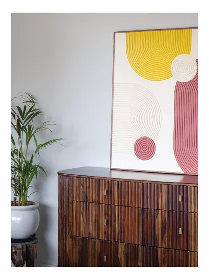 A corner of a bedroom in the 'Powai House', featuring a custom chest of drawers with a fluted wood finish. This piece provides essential storage while also serving as a beautiful stand for artwork, embodying our philosophy of functional art.