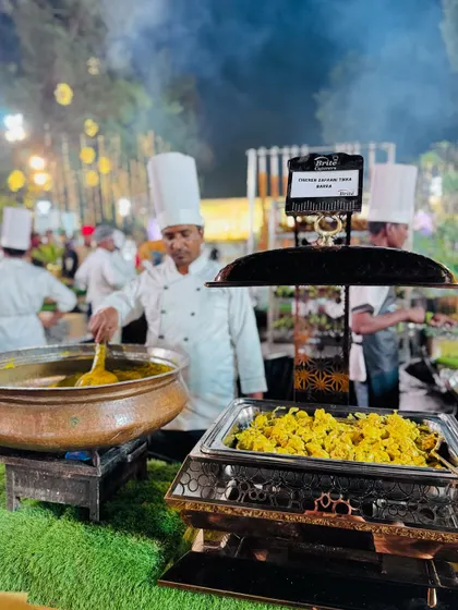 A chef stirs a large pot of curry next to the Chicken Zafrani Tikka Barra, illustrating a complete Mughlai food station.