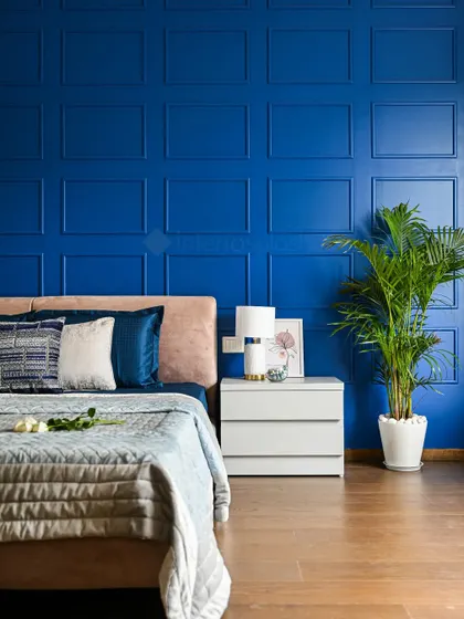 A close-up of the bedside in the royal blue room, highlighting the contrast between the bold wall and the soft, peach-colored headboard.