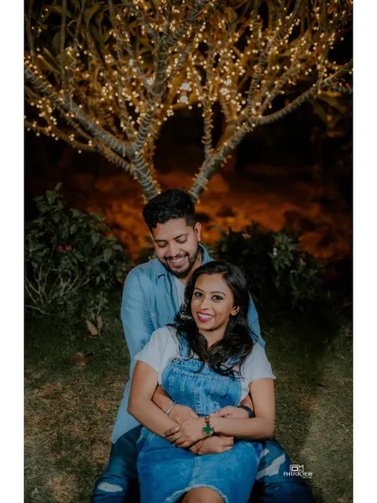 A sweet portrait of a couple sitting under a tree decorated with fairy lights.