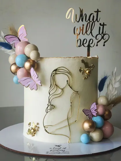 A beautiful and modern baby shower cake. The "What will it bee?" theme is subtly hinted at, with a line-art illustration of a mother-to-be, and a soft color palette of pastels and gold.