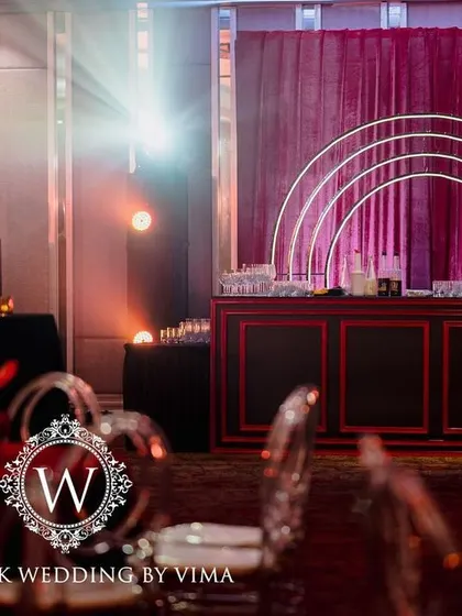 A bold and luxurious reception with a red and black color scheme. The decor includes rich red roses, modern crystal candelabras, and a stylish bar with a neon arch backdrop.