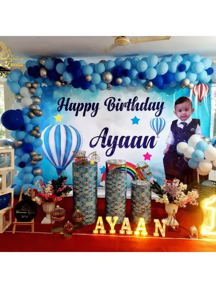 A hot air balloon themed first birthday party with a personalized photo backdrop and blue and silver balloons.