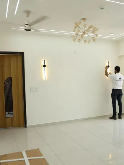 Our team member is installing modern wall lights in a spacious, empty living room. This image shows the blank canvas before furniture, highlighting the importance of getting the lighting and electricals right from the start.