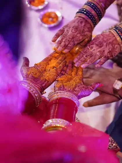 The joining of hands during a wedding ritual. This close-up shot, with its beautiful purple lighting, symbolizes the union of the couple and their families.