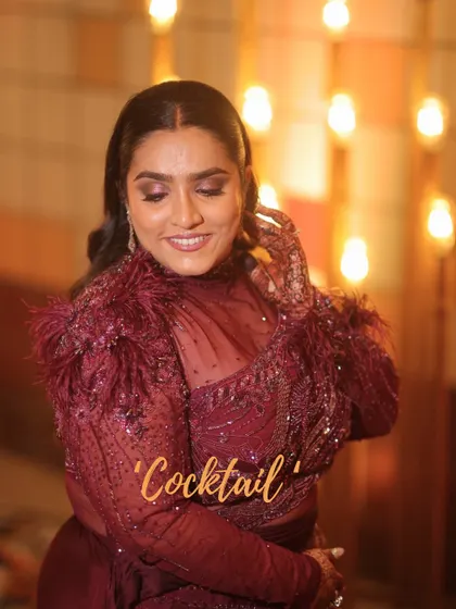A stunning cocktail look for a bride. The makeup is dramatic and bold, with smokey eyes and a deep berry lip that matches her feathered, wine-colored outfit perfectly.