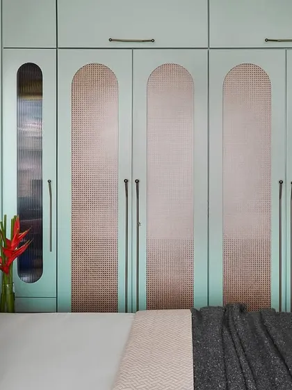 The wardrobe in the master bedroom features sage green shutters with cane inlays and capsule-like forms. This custom design adds a unique geometric pattern and accent to the room.