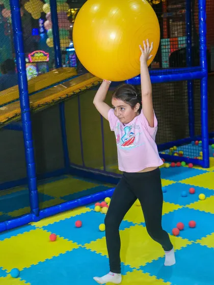 A girl showing her strength while playing with a large yoga ball in the play area.