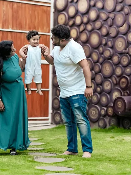 A beautiful family moment captured in our garden. The parents' loving gaze at their child, held up high, shows the pure joy of parenthood against our unique wooden log wall.