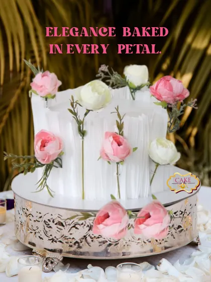 This unique pull-up cake features a delicate floral design, creating a moment of magic for any elegant event. The cake is surrounded by beautiful pink and white roses, set on an ornate silver stand.