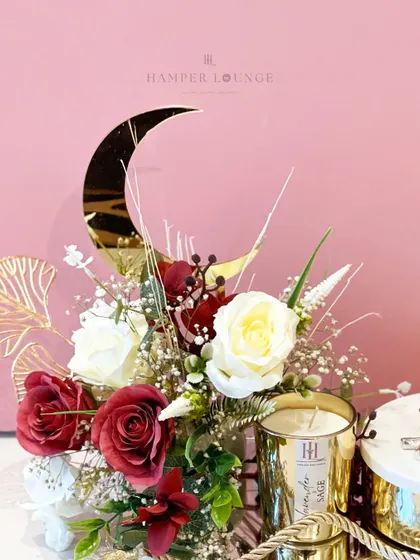 A detailed look at the mirrored tray Eid hamper, focusing on the golden crescent moon and the lush arrangement of red and white roses. The 'Lavender Sage' scented candle adds a touch of calming luxury.