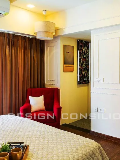 This master bedroom has a classic feel, with decorative molding on the walls and a comfortable red accent chair in the corner. The wooden flooring adds warmth to the space.
