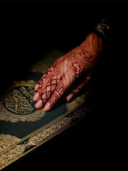 A beautifully lit close-up of the bride's henna-covered hand resting on the Quran, a symbolic and artistic detail shot.