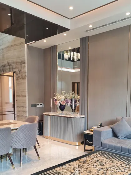 This image shows a custom-designed console with a ribbed base and marble top, placed strategically to define the entryway. The large mirror above it enhances the sense of space and reflects light, contributing to the room's open and airy feel.