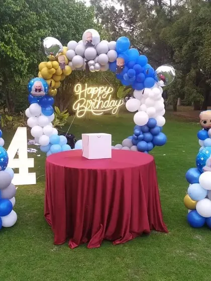 An outdoor Boss Baby themed 4th birthday party with a balloon arch and character cutouts.