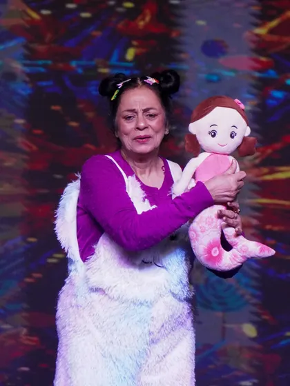 A participant in a playful costume holds a mermaid doll during her performance at Memorabilia.