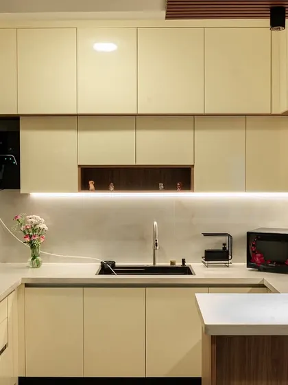A bright and modern U-shaped kitchen with cream-colored cabinets and a built-in chimney. The under-cabinet LED lighting illuminates the workspace and highlights the clean design.