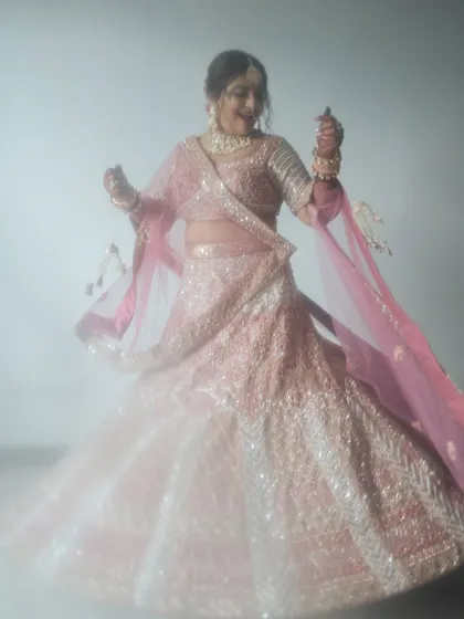 A dreamy, ethereal portrait of a bride in a pink lehenga. The soft focus and her twirling motion create a magical and romantic image.