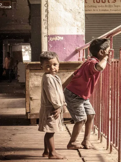 Two young children look out from a balcony, with one turning to gaze directly at the camera. This poignant street photograph captures the innocence and curiosity of childhood.