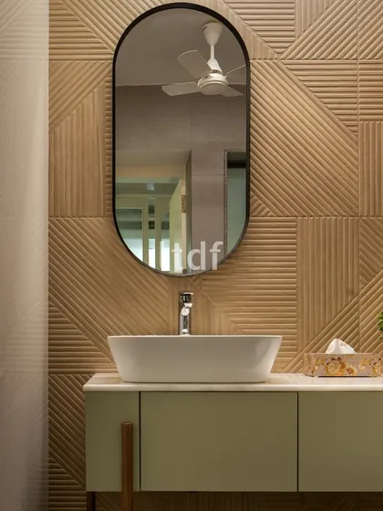 A detail of the clinic's powder room, where textured wall tiles in a warm wood tone create a sophisticated backdrop. The clean lines of the vanity and the elegant oval mirror contribute to a serene and modern aesthetic.