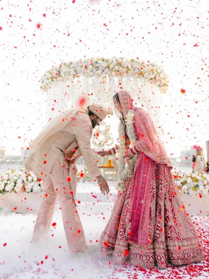 The moment of exchange during the varmala. The dynamic composition with the falling petals captures the energy and excitement of the ceremony.